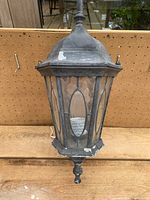 Front view of black carriage-style outdoor light showing ornamental textured glass panels and wear on black finish.