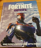 Front cover of the official Fortnite Outfits Collectors' Edition hardcover book showing a futuristic armored character and title text.