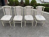 Four beige metal frame kitchen chairs with padded seats and backs, arranged in a row outside on pavement, showing overall wear.