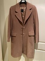 Full front view of beige wool and cashmere coat on hanger showing three-button closure, notch lapels, and two flap pockets.