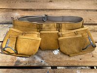 Front view of the heavy-duty leather carpenter’s belt showing multiple pouches and metal hammer hangers on a wooden surface.