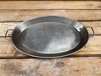 Top-down view of oval metal serving tray with handles on a wooden surface to show shape and size.