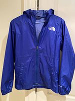 Front view of blue North Face rain jacket with hood, zipper closure, and logo on upper left chest.
