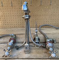 Wide shot of faucet spout and both hot and cold tap assemblies with hoses and mounting hardware on workbench