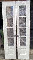 Front view of two custom Madawaska pocket doors wrapped in plastic showing four glass panels and bottom panel relief design.