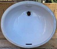 Top view of white porcelain oval undermount sink showing drain hole and overflow slot