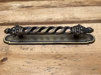 Close-up of a brass drawer pull with twisted basket weave design mounted on a wooden surface.