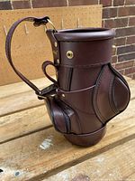 Full view of the brown leather-like wine bottle holder with golf bag shape on wooden surface