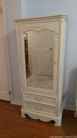 Full view of cream-colored manufactured wood armoire showing mirrored door and two drawers.