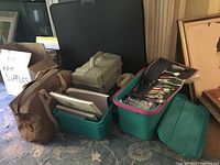 Overall view of art supplies including storage tubs, canvas boards, art portfolio carrier, and brushes.