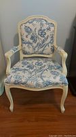 Frontal image of cream framed armchair with blue floral upholstery on seat and backrest, showing overall condition and design.