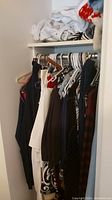 Closet rod with multiple pieces of women's clothing including skirts, sweaters, tops, and pants in dark, white, and patterned fabrics.