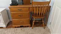 View of the desk's left drawer bank with three brass handled drawers and matching wood chair with spindle back.