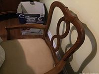 Close-up photo showing the wooden chair back with decorative cutouts and beige upholstered seat.