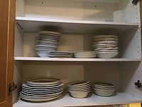 Shelves with stacked assorted dishes including dinner plates, bowls, and side plates, some showing chips and wear