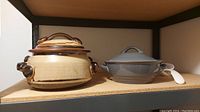 View of both fondue pot and Dansk covered casserole dish with ladle on shelf.