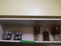 Six large brown tinted glass water goblets on a shelf