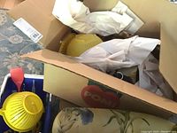 Open box containing a yellow plastic colander and other kitchen items packed inside paper