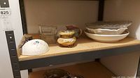 Shelf with white ceramic trinket box, yellow creamer and sugar set, white serving bowls and platters, clear Pyrex loaf pans