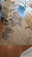 Area carpet rug placed on wooden floor showing overall floral pattern, beige and gray tones visible
