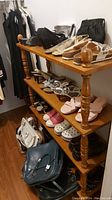 Full view of the four tiered wooden shelf unit with various shoes and purses on the shelves to indicate scale. The wood is medium brown with turned legs.