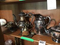 Silver plated coffee pot, tea pot, water pitcher, tray on shelf with small cleaning brush and spoon