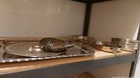 Silver-plated trays and bowls arranged on a shelf showing different styles and sizes.