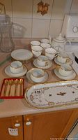 Overview of teacups, saucers, plates, teapot, and platter on a countertop showing gold trim and floral designs