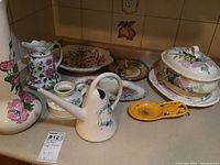 Full lot view showing all items including covered vegetable dish with matching tray, ceramic watering can, enamel iron spoon rest, various bowls and jugs clustered on counter.