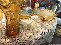 Tall amber glass vase with wavy rim, amber and frosted glass candy dish, clear glass footed tray and candle holders on lace tablecloth