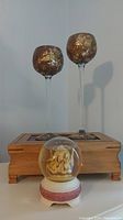 Photo showing water globe music box, wooden box with hinged lid behind it, and pair of tall glass candle holders with gold tops.