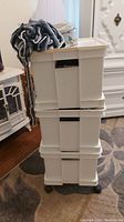 Photo of the white three-drawer plastic storage bins stacked on a wheeled black frame, with a yarn bundle and a round decorative tin on top.