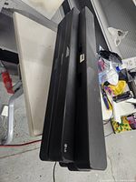 Image showing multiple black LG sound bars stacked on a white table in a workshop setting.