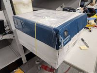 Box of Business Source branded copy paper on a workbench, sealed with plastic and yellow rubber band