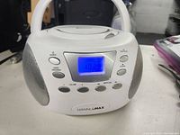 Front view of white Hannlomax boombox showing blue digital display and control buttons.