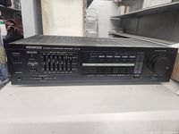 Front view of Kenwood KA-75 amplifier showing power button, graphic equalizer sliders, input selection, and large volume control knob.