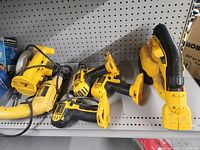 Four Dewalt cordless and corded tools on a metal shelf, including a reciprocating saw, jigsaw, drill driver, and vacuum cleaner.