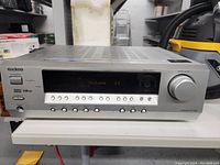 Front view of Onkyo AV Receiver HT-R340 on white surface showing power button, LED display with volume display, speaker selector, headphone jack, surround sound logos and input selection buttons.