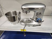 Full view of silver Posame stand mixer showing its base, control dial, power cord and included stainless steel mixing bowl placed beside it on the shelf.