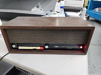 Front-right perspective showing wood veneer case, cloth speaker grill and illuminated red LED.