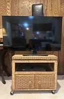 40-inch TCL Roku flat screen TV placed on top of a wicker TV stand on wheels with cabinet below. Includes Samsung DVD player on shelf.