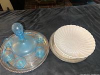 Blue hand-blown glass decanter with stopper and six matching glasses arranged on an ornate silver tray, alongside white serving bowls.
