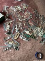 Overview of costume jewelry pieces in plastic bags laid on carpet, containing earrings and necklaces