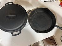 Top view of cast iron Dutch oven pot with lid and cast iron frying pan side by side showing size and shape.