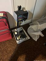 Full view of the Omega Chromega B Dichroic darkroom photo enlarger on baseboard with accessories beside a red suitcase.