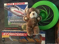 Lot containing Data Becker Private Wings box, America Jet Fighters diecast aircraft in packaging, green frisbee, and brown plush teddy bear.
