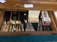 Photo showing drawer with a large goldtone Cambridge stainless steel flatware set with knives, forks, spoons, Janis Collection cheese cutting tools in box, coasters, and assorted candles.