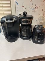 Photo of three kitchen appliances: Keurig K-Classic coffee maker, Mr. Coffee programmable coffee maker, and Oster 4-slice toaster on kitchen counter.