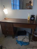 Front view of MCM wooden desk with desk lamp on left side, showing desk drawers and items on desktop.