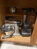 Photo showing Ninja blender and Mixmaster stand mixer inside wooden cabinet shelf.